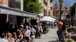 Menschen sitzen auf der Terrasse eines Restaurants am Fluss Thiou in der Altstadt. Annecy, Frankreich. Symbolfoto.