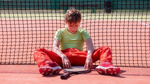 Der Junge hat den Tenniswettbewerb verloren. Das Kind sitzt mit einem Schläger am Netz.   