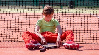 Der Junge hat den Tenniswettbewerb verloren. Das Kind sitzt mit einem Schläger am Netz.   