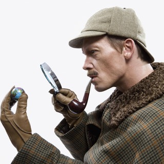 Ein als Sherlock Holmes verkleideter Mann betrachtet einen winzigen Globus durch eine Lupe.