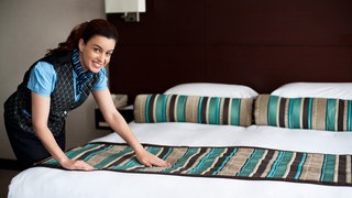 Elegant housekeeping lady adding final touches to bedroom before customer arrival . Symbolfoto.