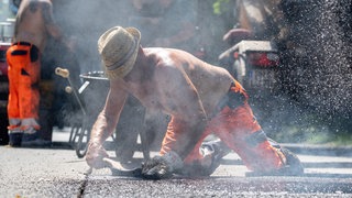 Asphaltbauer belegen bei 33 Grad in der Mittagssonne in Potsdam eine Straße mit 210 Grad heißem Gussasphalt.