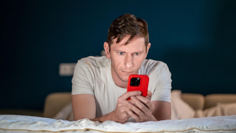 Ein Mann benutzt sein Smartphone auf dem Bett liegend