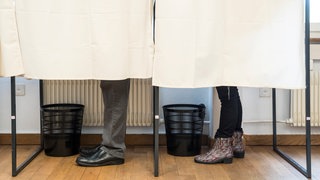 Zwei Personen in zwei Wahlkabinen (Symbolbild)