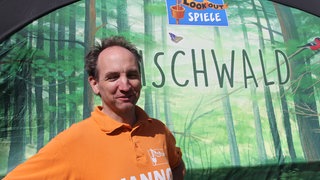 Lookout-Games-Geschäftsführer Hanno Girke vor einem Aufsteller zum Spiel "Mischwald"