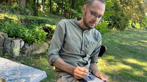 Daniel Beerstecher sitzt schweigend im Garten des Klosters Neustadt an der Weinstraße und notiert etwas auf seiner Tafel