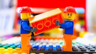 Zwei Lego Bau Arbeiter tragend zusammen einer Orangefarbene Backstein 