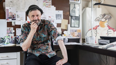 Ralf König, Comicautor und Zeichner, sitzt in seinem Atelier. 
