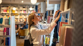 Frau stöbert durch Regale in Buchhandlung 