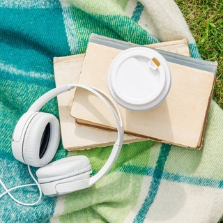 Bücher, Kopfhörer und Kaffee liegen auf einer Picknickdecke in einer Wiese