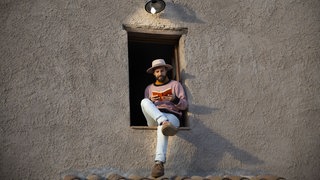 Mann mit Buch im Fensterrahmen sitzend, lesenswert Magazin 31.05.2026