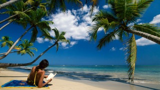 Eine Frau liest ein Buch an einem karibischen Strand.