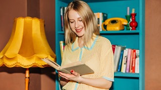 Lächelnde Frau, die in einem farbenfroh gestalteten Raum ein Buch liest
