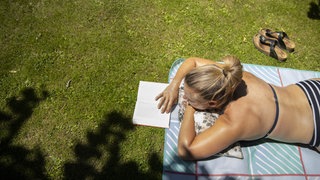 Eine junge Frau liegt auf einer Picknickdecke und liest ein Buch.