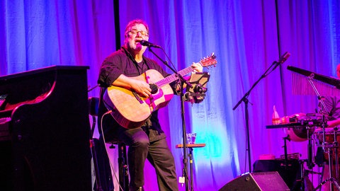 Klaus Lage steht mit einer Gitarre auf der Bühne und singt.