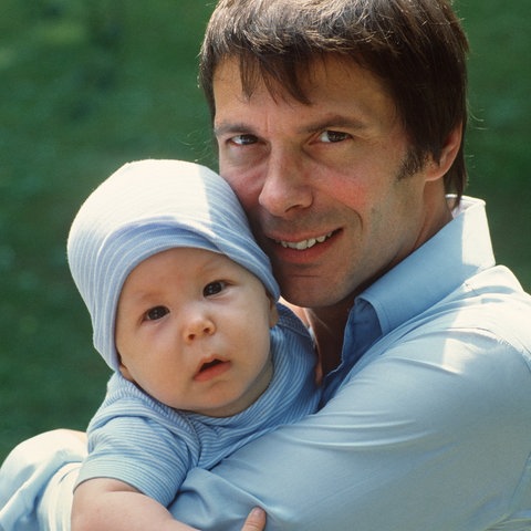 Der deutsche Sänger Reinhard Mey ("Über den Wolken") hält seinen kleinen Sohn Max auf dem Arm und lächelt in die Kamera (1982)