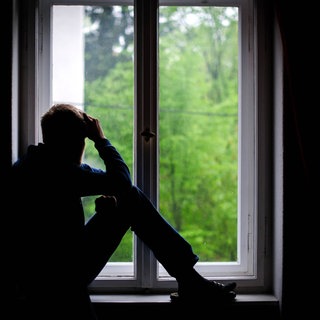 Symbolbild Einsamkeit: Ein Mann sitzt alleine an einem Fenster und schaut nach draußen
