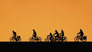 Fahrradfahrer silhouettiert vor dem orangefarbenen Sonnenuntergangshimmel im Sommer