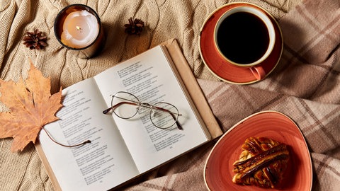 aufgeschlagenes Gedichtbuch mit Brille, Kaffeetasse, Zimtschnecke und Kerze