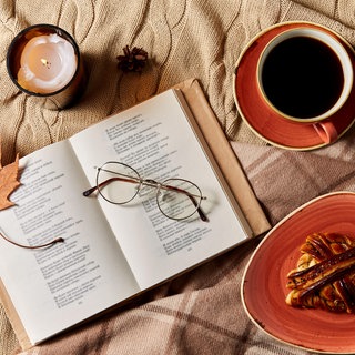 aufgeschlagenes Gedichtbuch mit Brille, Kaffeetasse, Zimtschnecke und Kerze