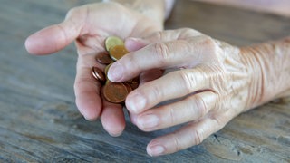 Hände einer älteren Frau zählen Münzen am Tisch