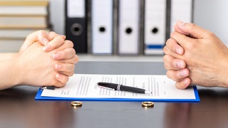 Ehepaar sitzt vor Ehevertrag mit Ehehringen auf dem Tisch