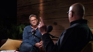 Christian Peter Dogs zeigt mit dem Finger auf die Decke, während Florian Weber zuhört