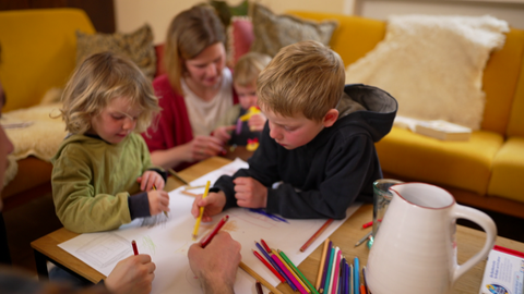 Drei kleine Jungs beugen sich über ein großes Blatt Papier und malen.