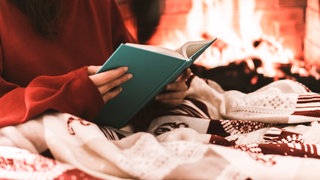 Frau liest ein Buch vor dem Kamin