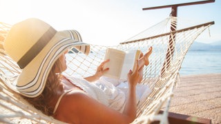 Frau liegt in einer Hängematte und liest ein Buch