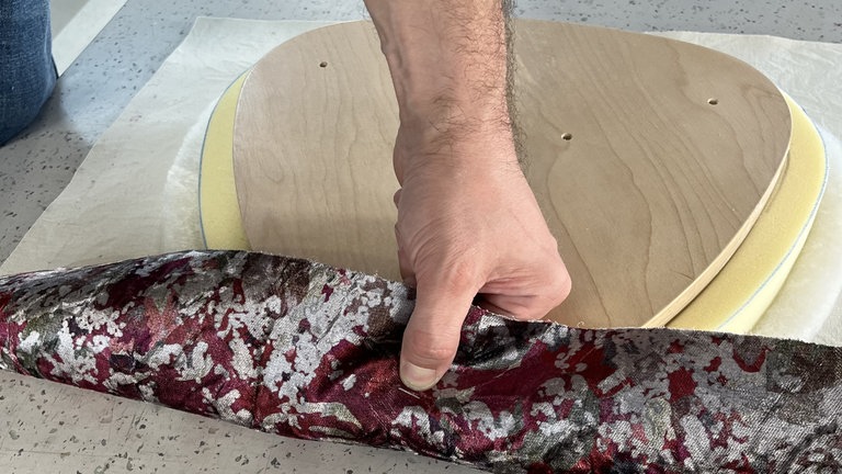 Zug auf den Stoff ausüben, bis unter der Hand die Holzkante spürbar wird. An der Spitze einen Heftschuss anbringen, die Klammer wird schräg geschossen, damit sie anschließend problemlos wieder entfernt werden kann.