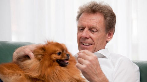 Ein älterer Mann streichelt einen Hund.