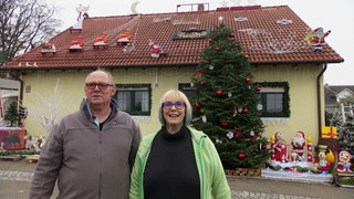 Ehepaar steht vor weihnachtlich geschmücktem Haus