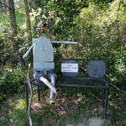 Ein Troll sitzt auf einer Bank im Wald auf dem Trollpfad im Mittelrheintal.