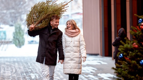 Paar läuft Hand in Hand und Mann trägt einen Tannenbaum