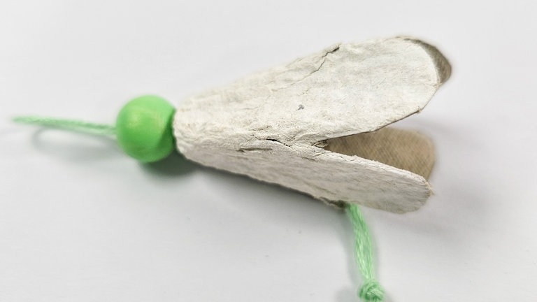 die Schnur durchziehen und die Fadenenden zu einem dicken Knoten verknoten. An der Schlaufe ziehen, sodass sich der Knoten in die Blüte hineinzieht.
