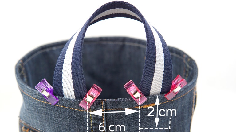 Das Webband in zwei 30 cm lange Stücke teilen und die Schnittkanten mit Zickzackstich versäubern (bei Kunstfaser kann man die Kanten auch vorsichtig mit einem Feuerzeug verschmelzen). Den ersten Henkel wie abgebildet an den inneren Korbrand heften.