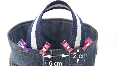 Das Webband in zwei 30 cm lange Stücke teilen und die Schnittkanten mit Zickzackstich versäubern (bei Kunstfaser kann man die Kanten auch vorsichtig mit einem Feuerzeug verschmelzen). Den ersten Henkel wie abgebildet an den inneren Korbrand heften.