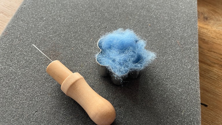 Zu Beginn wird ein Ausstecher in Blumenform benötigt, sowie die erste Blütenfarbe. Ein ordentliches Stückchen Filzwolle abzupen und in die Form drücken. 