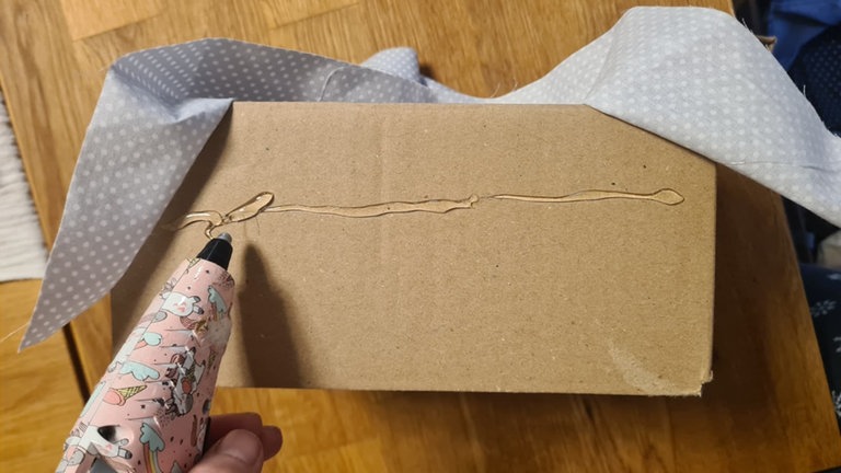 Anschließend die Innenmaße der Box mit dem Lineal anlegen und ein passendes Stück Stoff oder Filz zuschneiden, das etwas über den Rand hinausragt. Dieses Stoffstück in die Box legen, glatt streichen und am oberen Rand mit Kleber befestigen, damit keine Falten entstehen. 