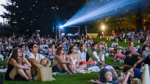 Zuschauer verfolgen einen Film auf großer Leinwand bei einem Open-Air-Kino unter freiem Himmel.