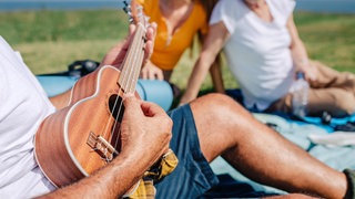 Ein Mann sitzt auf einer Wiese und spielt Ukulele | Warum mehr Erwachsene ein Instrument lernen sollten