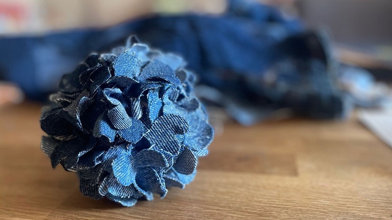 Die kleinen Jeansblüten zu Kelchen formen und mit Heißkleber auf der Kugel festkleben. Während der Kleber heiß und flüssig ist, lassen sich die Kelche durch zusammendrücken gut formen.