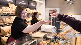 Bäckereifachverkäuferin nimmt in einer Bäckerei Bargeld entgegen