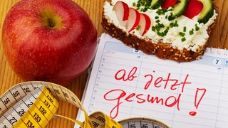 Kalender mit den Worten "Gesunde Ernährung" mit Maßband, Obst und Brot