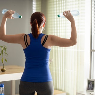 Fünf-Minuten-Fitness: Frau trainiert Schulter mit Wasserflaschen