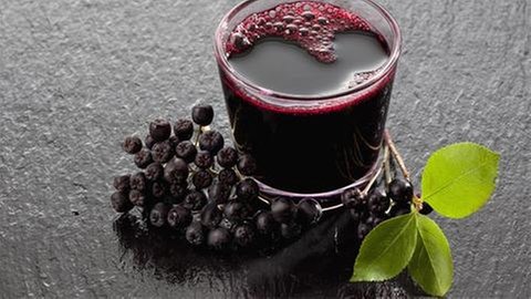 Aroniasaft in einem Glas, daneben Beeren mit Blättern