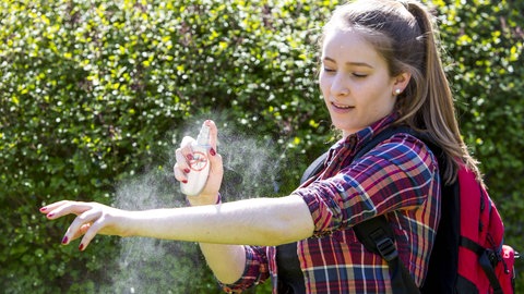 Junge Frau trägt Mückenschutz auf - das Spray hilft auch gegen Grasmilben