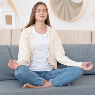 Frau sitzt auf Couch im Yogasitz