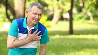 Ein älterer Mann greift sich mit schmerzverzerrtem Gesicht an den Brustkorb im Bereich des Herzens. Das kann ein Symptom für eine Aortenaneurysma - erweiterte Hauptschlagader - sein.